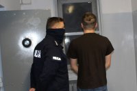 umundurowany policjant prowadzi zatrzymanego do celi w pomieszczeniu dla osób zatrzymanych w wieluńskiej komendzie