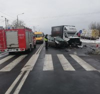 umundurowany policjant pracujący na miejscu wypadku drogowego. Na drodze znajdują się trzy uszkodzone samochody, które uczestniczyły w zdarzeniu. Z boku wóz strażacki.