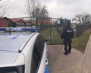 radiowóz oraz umundurowany policjant przed bramą wejściową na teren ogródków działkowych