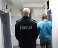 umundurowany policjant prowadzi do celi zatrzymanego.