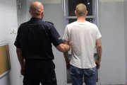 umundurowany policjant prowadzi zatrzymanego do celi