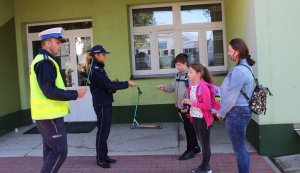 umundurowani policjanci przed szkołą wręczają dzieciom odblaski