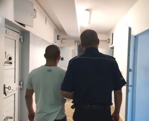 umundurowany policjant prowadzi zatrzymanego do celi w pomieszczeniu dla osób zatrzymanych