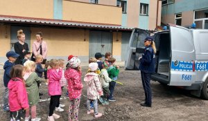 policjantka przed budynkiem komendy prezentuje dzieciom radiowóz