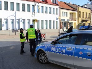 policjanci wręczaj elementy odblaskowe przechodniom w tle stoi radiowóz