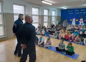 policjanci w sali gimnastycznej prowadzą pogadankę z dziećmi które siedzą na przeciwko