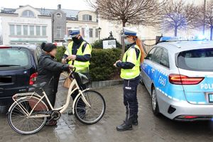 policjant i policjantka ruchu drogowego wręczają element odblaskowy rowerzystce, obok stoi radiowóz