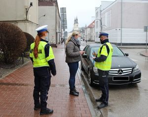 policjant i policjantka ruchu drogowego wręczają element odblaskowy pieszej