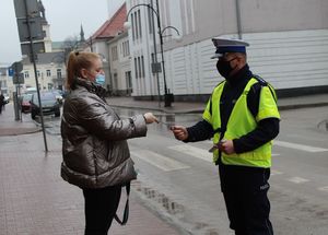 policjant i policjantka ruchu drogowego wręczają element odblaskowy pieszej