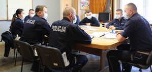 policjanci siedzą przy stole podczas odprawy z Naczelnikiem Wydziału Ruchu Drogowego