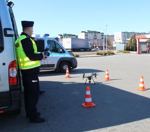 policjant stoi na parkingu i  obsługuje policyjnego drona
