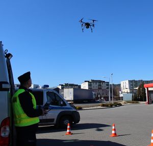 policjant stoi na parkingu i  obsługuje policyjnego drona, który leci w powietrzu