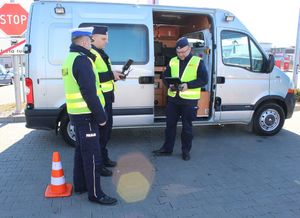 policjanci stoją na parkingu i  obsługują policyjnego drona
