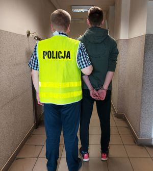 policjant prowadzi zatrzymanego po korytarzu komendy