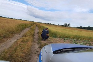 umundurowany policjant na polu w miejscu gdzie znaleziono niewybuch. Z przodu widoczny element przodu radiowozu.