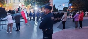 Policjant stoi na ulicy pośród zgromadzonych uczestników  obchodów rocznicy  wybuchu II Wojny Światowej.