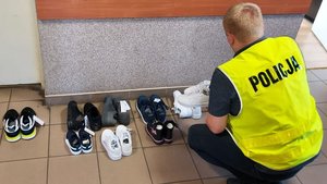 Policjant w kamizelce z napisem Policja na korytarzu dokonuje oględzin zabezpieczonego obuwia pochodzącego z kradzieży.