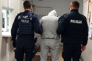 Umundurowani policjanci prowadzą zatrzymanego po korytarzu komendy policji.