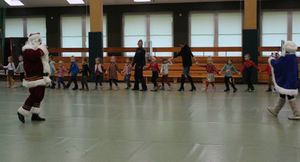 Mikołaj stoi na środku sali gimnastycznej, policjantka i dzieci tańczą wokoło.