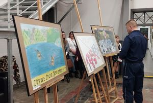 W sali Dworca Kulturalnego Wieluń Dąbrowa po boku stoją nagrodzone prace plastyczne oraz policjant oglądający prace.