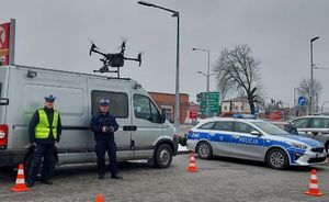 Dwaj policjanci stoją na parkingu, jeden z nich obsługuje drona, który unosi się w powietrzu.