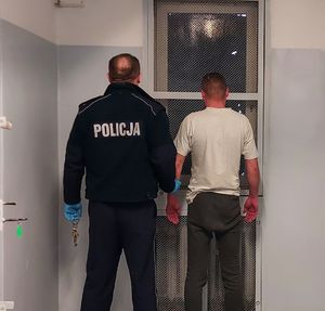 Policjant prowadzi zatrzymanego do celi w pomieszczeniu dla osób zatrzymanych.