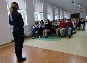 Policjantka stoi w sali i prowadzi pogadankę z dziećmi, które siedzą naprzeciwko.