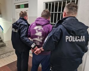 Policjanci prowadzą zatrzymanego w kajdankach po korytarzu w budynku komendy.