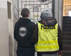 Policjant prowadzi zatrzymanego po korytarzu w budynku komendy.