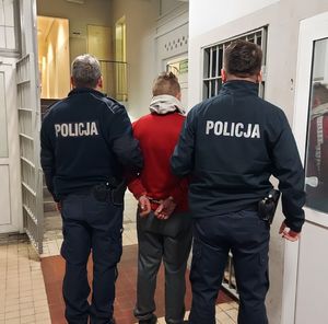Policjanci prowadzą zatrzymanego po korytarzu w budynku komendy.