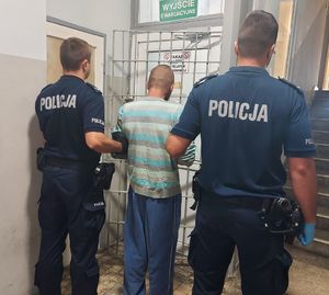 Policjanci prowadzą zatrzymanego po korytarzu w budynku komendy.