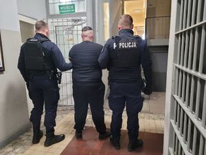 Policjanci prowadzą zatrzymanego po korytarzu budynku komendy.