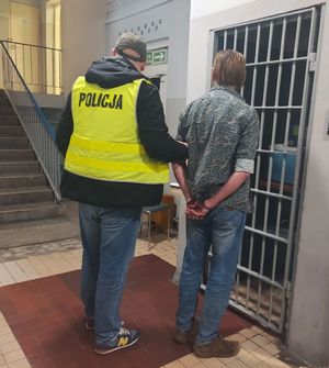 Policjant prowadzi zatrzymanego po korytarzu w budynku komendy.