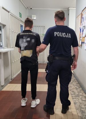 Policjant prowadzi zatrzymanego po korytarzu w budynku komendy.