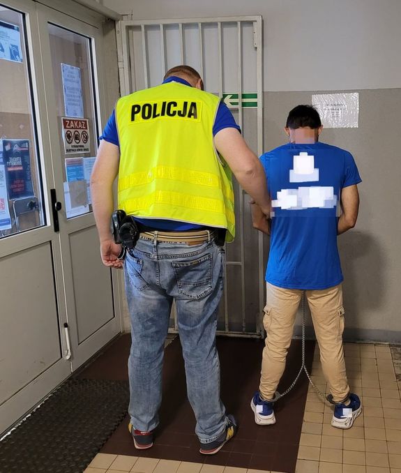 Policjant prowadzi zatrzymanego po korytarzu w budynku komendy.