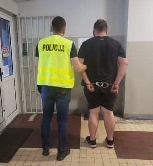 Policjant prowadzi zatrzymanego po korytarzu w budynku komendy.