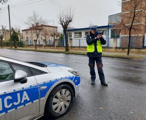 Radiowóz stoi na poboczu, policjant używa miernika prędkości.