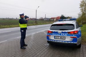 Radiowóz stoi na poboczu, policjant używa miernika prędkości.