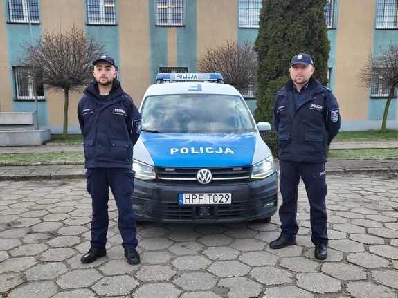 Umundurowani policjanci stoją przy radiowozie.