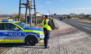 Radiowóz, stoi przy nim policjantka, która trzyma w ręku miernik prędkości.