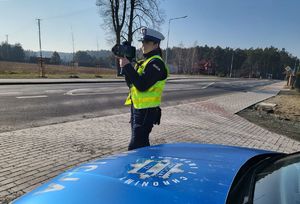 Maska radiowozu i stojąca przy nim policjantka mierząca prędkość.