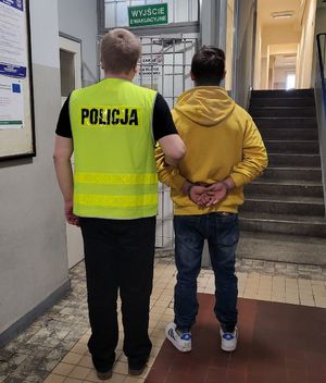 Policjant prowadzi po korytarzu w budynku komendy zatrzymanego.