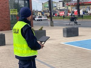 Policjant na parkingu przy drodze operuje dronem przeznaczonym do ujawniania wykroczeń i przestępstw drogowych.