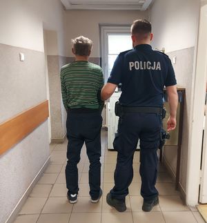 Policjant prowadzi zatrzymanego po korytarzu w budynku komendy.