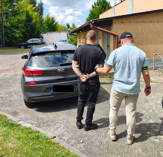 Policjant prowadzi zatrzymanego do auta.