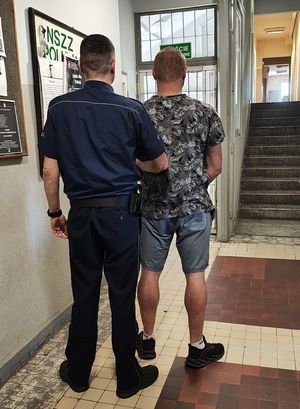 Policjant prowadzi zatrzymanego po korytarzu w budynku komendy.