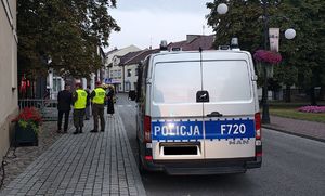 Radiowóz policyjny stoi przy drodze, w tle stoją żołnierze.