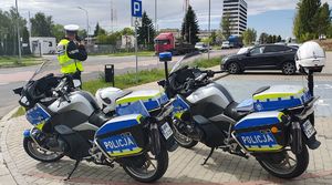 Policjant mierzy prędkość poruszających się pojazdów , z boku na  parkingu stoją dwa policyjne motocykle.