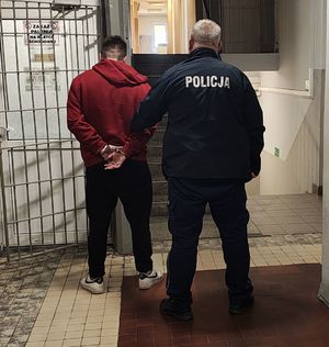 Policjant prowadzi zatrzymanego po korytarzu w budynku komendy.