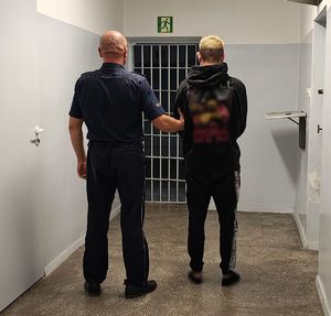 Policjant prowadzi zatrzymanego po korytarzu w pomieszczeniu dla osób zatrzymanych.